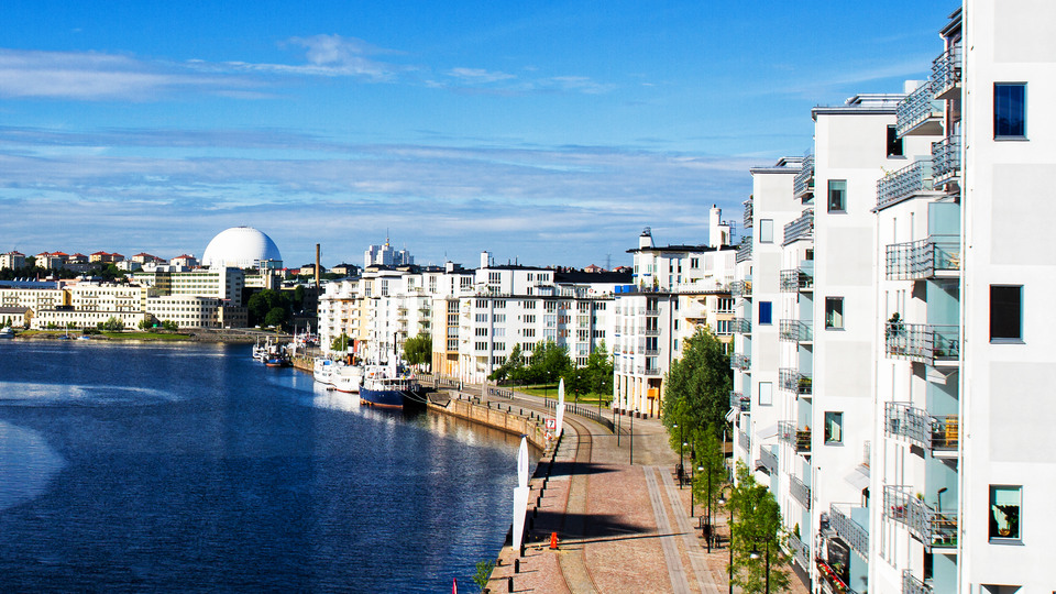 New and modern settlement in Stockholm, Sweden.  Big white apartment complex right by the water, a view of Globen in the distance.