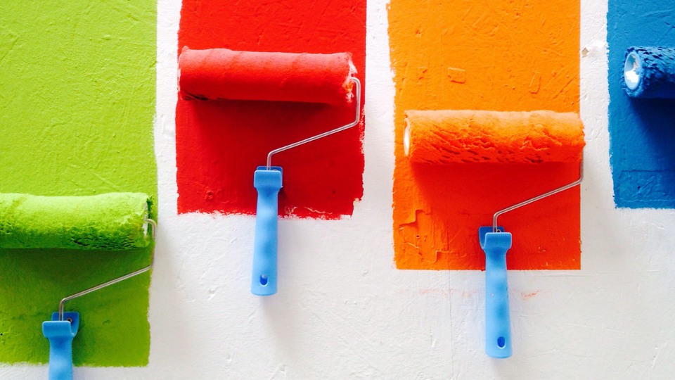 Strips of green, red, orange and blue wall paint, with a roller at the bottom of each color.