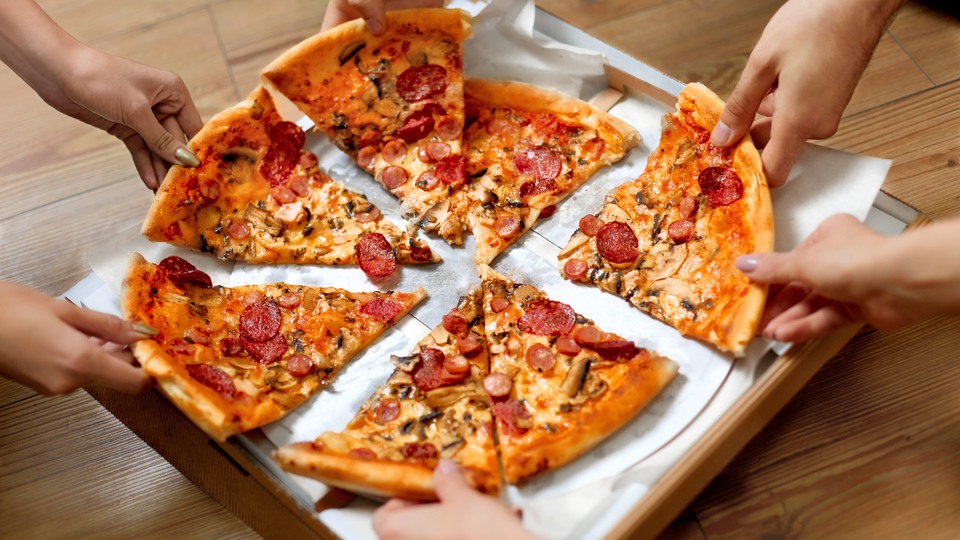 Flera personer dela på en pizza som ligger i en kartong
